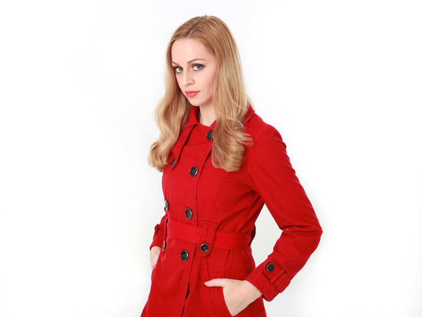 πορτρέτο του όμορφη ξανθιά κοπέλα φορώντας κόκκινο παλτό χαράκωμα. απομονωμένα σε φόντο λευκό στούντιο. - Φωτογραφία, εικόνα