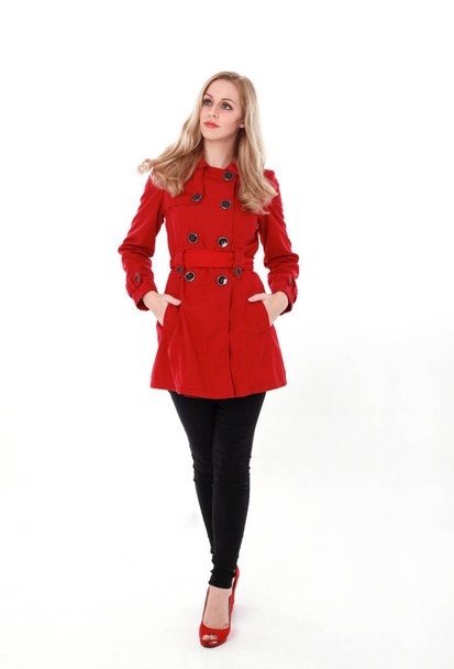 全身立ちポーズの赤いトレンチ コートを着てかなりブロンドの女の子の肖像画.ホワイト スタジオの背景に分離. - 写真・画像