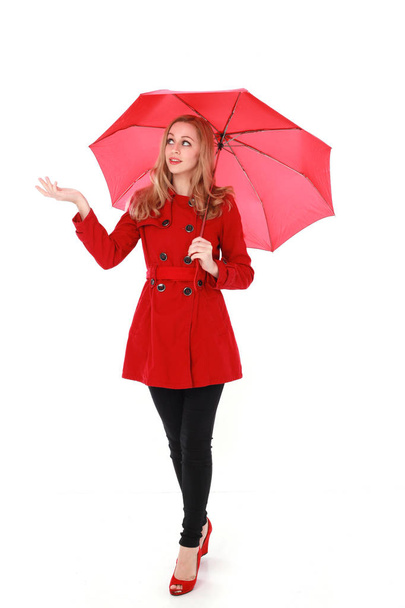 portrait of pretty blonde girl wearing red trench coat, holding an umbrella. full length standing pose. isolated on white studio background. - Photo, image