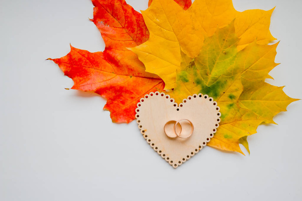 Wedding ring on wooden heart on autumn leaves background. Close-up view of golden wedding rings. Autumn wedding card or wedding invitation. Colorful maple leaves.Copy space - Foto, immagini