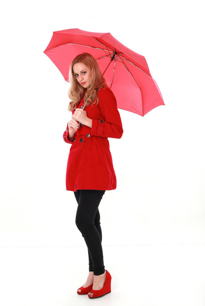 portrét hezká blondýnka dívka, která nosí červený plášť, držící deštník. po celé délce stojící pozice. izolované na bílém studio pozadí. - Fotografie, Obrázek