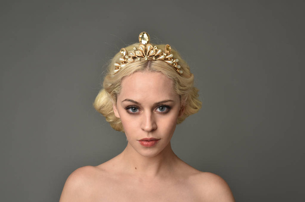 portrait of blonde woman wearing golden crown, grey studio background. - Photo, Image