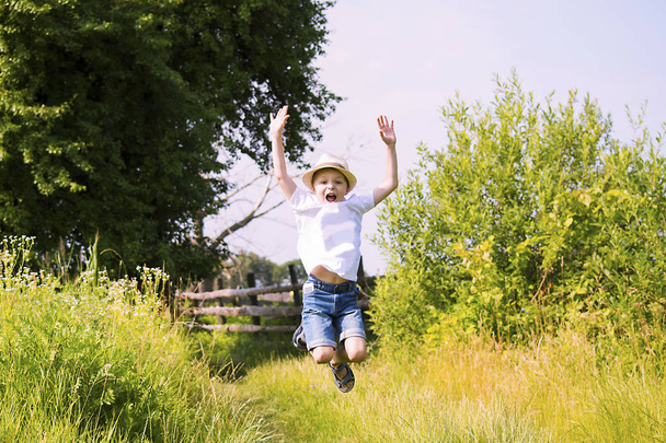 happy cute boy jumping high on nature in the village in summer - Foto, afbeelding