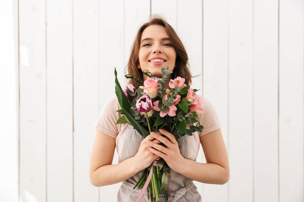 Young cute happy florist woman standing with flowers in workshop. - Fotó, kép