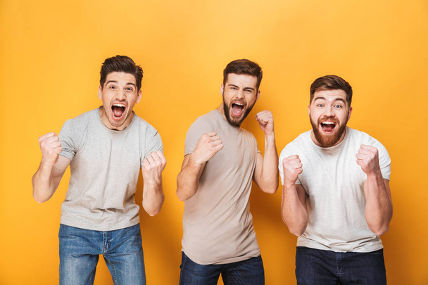 Three young excited men celebrating success together isolated over yellow background - Fotó, kép