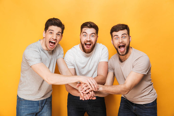 Three young joyful men celebrating success together isolated over yellow background - Foto, immagini
