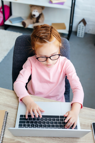 overhead view of focused red haired schoolchild using laptop at desk - Foto, Bild