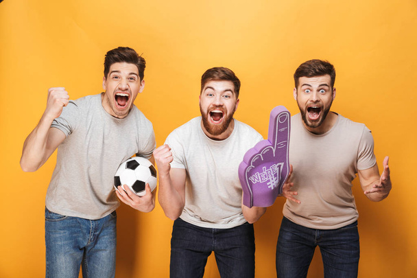 Three young cheery men football fans celebrating isolated over yellow background - Foto, Bild