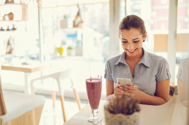 Smartphone kullanarak ve meyve yüzlü içme genç gülümseyen iş kadını - Fotoğraf, Görsel