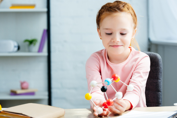 krásnou usměvavou školačka sedí u stolu a držení molekulární model - Fotografie, Obrázek