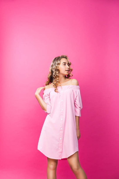 Pretty stylish girl with long curly hair wearing beautiful pink dress and posing against pink background. Fashion vogue style portrait of young happy smiling woman, copy space. - Photo, Image
