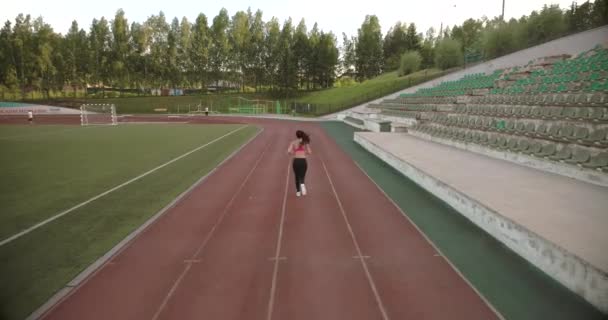 aerial. jogging. sports girl running through the stadium. back view - Footage, Video