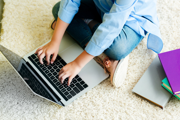 Schnappschuss eines kleinen Kindes, das auf Teppich sitzt und zu Hause Laptop mit leerem Bildschirm benutzt  - Foto, Bild