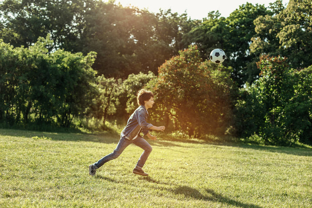 Aufgeregter Junge rennt in der Natur dem Ball hinterher - Foto, Bild