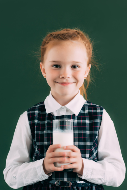 adorable colegiala sosteniendo un vaso de leche y sonriendo a la cámara
   - Foto, imagen