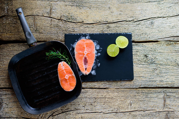 Two salmon steaks are ready to cook on a grill, along with lime on a wooden background. Top view. Healthy food. - Фото, зображення