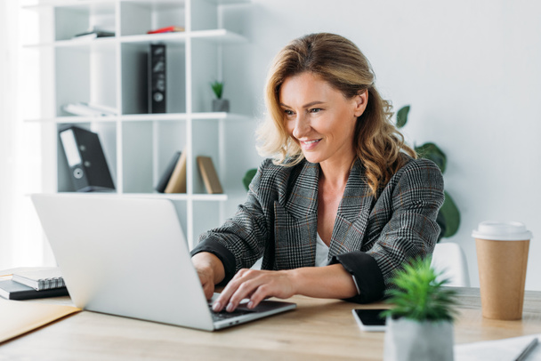 Attractive businesswoman working on laptop in office - Photo, Image