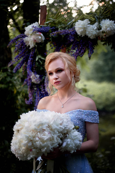 The bride stands at the arch, decorated with flowers, with a large bouquet of white peonies.On-site registration in the Park Wedding walk and photo shoot - Fotografie, Obrázek