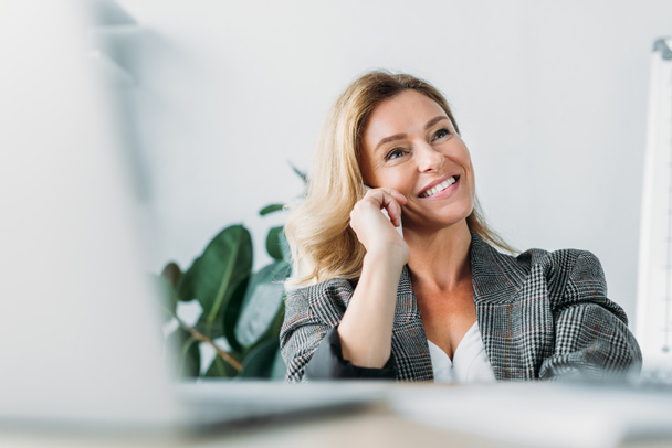 smiling attractive businesswoman talking by smartphone in office - Foto, Bild