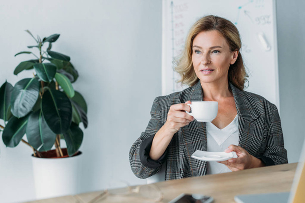 attractive businesswoman holding cup of coffee in office - Фото, зображення
