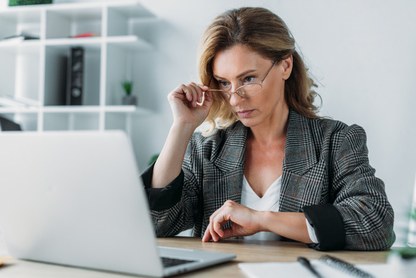 mulher de negócios atraente olhando para laptop no escritório
 - Foto, Imagem