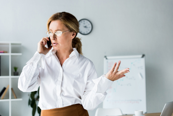 Attraktive Geschäftsfrau spricht per Smartphone und gestikuliert im Büro - Foto, Bild