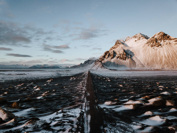 A road leading towards a mountain through a snow covered landscape in Stokksnes, Iceland. The photo is taken using a drone. - Foto, imagen