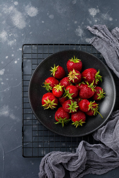Fresh strawberries on black plate on dark old concrete background. Top view. - Foto, afbeelding