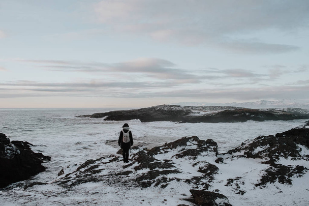 Une personne marche sur des falaises enneigées au bord de la mer à Stokksnes, Islande
 - Photo, image