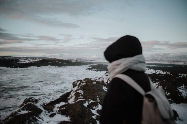 Ένα άτομο που στέκεται πάνω σε κάποια βράχια, κοιτάζοντας πάνω από τη θάλασσα στην Stokksnes, Ισλανδία. - Φωτογραφία, εικόνα
