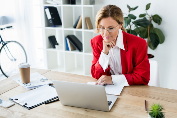 mulher de negócios atraente olhando para laptop no escritório
 - Foto, Imagem