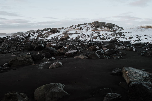 Rocas en una playa de arena negra frente a un paisaje nevado en Stokksnes, Islandia
. - Foto, imagen