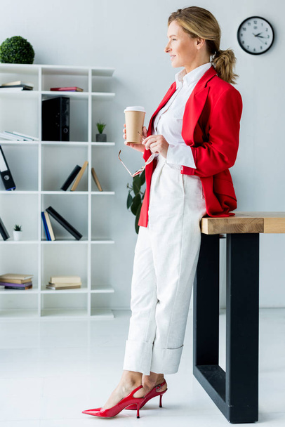 side view of beautiful businesswoman standing with coffee in paper cup in office - Fotografie, Obrázek