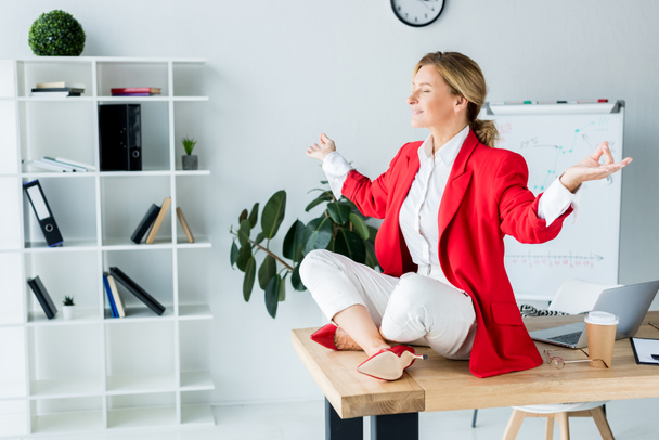 attractive businesswoman meditating in lotus pose on table in office - Foto, imagen