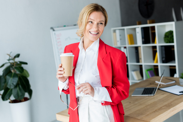 mulher de negócios atraente de pé com café no copo de papel no escritório
 - Foto, Imagem