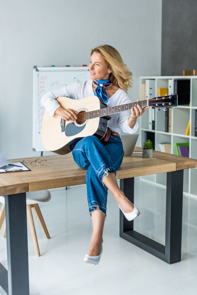 smiling attractive businesswoman playing acoustic guitar in office - Foto, afbeelding