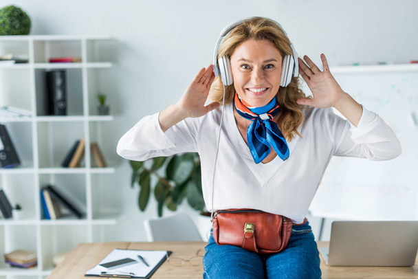 attractive happy businesswoman listening music in headphones in office - Фото, изображение