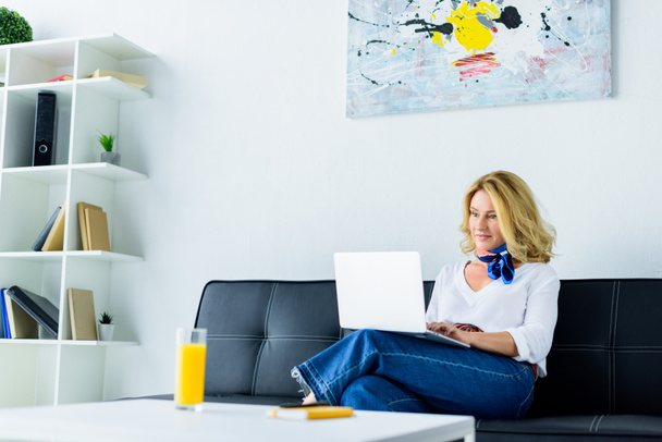 attractive businesswoman sitting on sofa in office and working with laptop - Fotografie, Obrázek