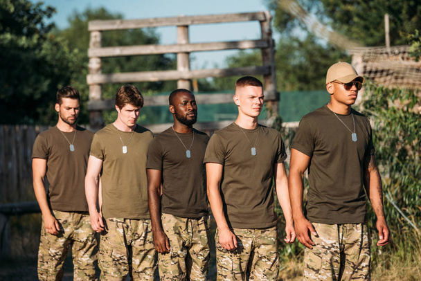 wielonarodowa Grupa młodych żołnierzy w mundurach wojskowych z psami tag, stojąc na zakres - Zdjęcie, obraz