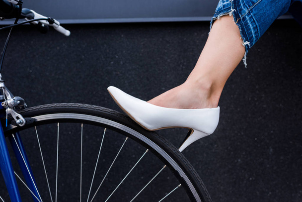 imagen recortada de mujer en zapato blanco tocando rueda de bicicleta en la calle
  - Foto, Imagen