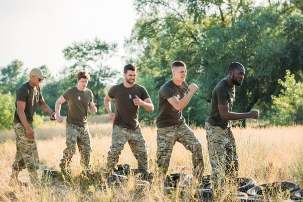 Zijaanzicht van Sex tussen verschillendre rassen soldaten oefenen met banden op grond op bereik - Foto, afbeelding