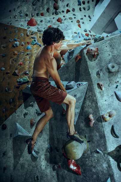 Free climber young man climbing artificial boulder indoors - Fotó, kép