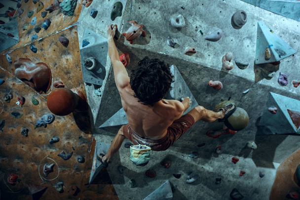 Free climber young man climbing artificial boulder indoors - Foto, afbeelding