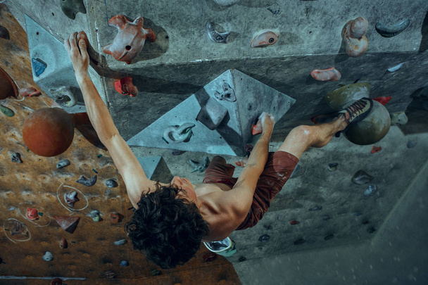 Free climber young man climbing artificial boulder indoors. Climbing concept and extreme activity. The young fit man on rock - Foto, immagini
