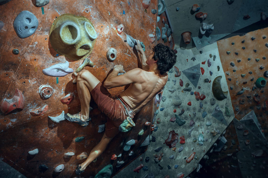 Free climber young man climbing artificial boulder indoors - 写真・画像