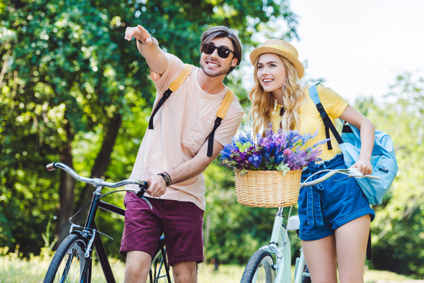 portrait of young couple with backpacks and bicycles in park - Photo, Image