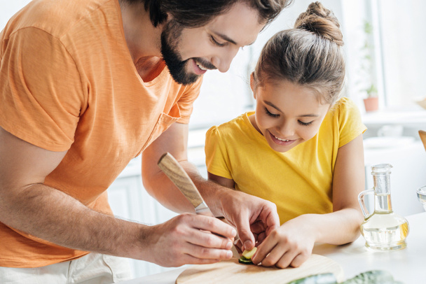 padre e hija tallando pepino mientras cocinan juntos en casa
 - Foto, Imagen