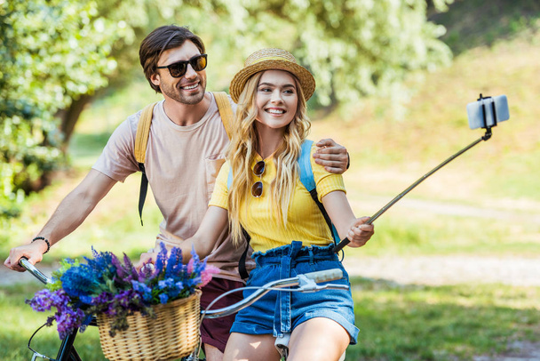 smiling couple in love with bicycles taking selfie in park on summer day - Photo, Image