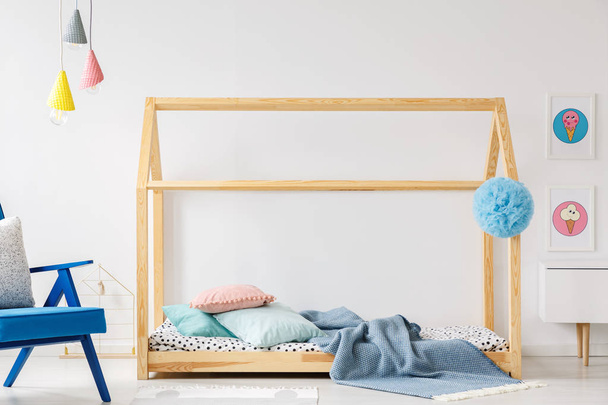 Wooden DIY bed in modern child's bedroom interior with blue armchair and posters - Photo, image