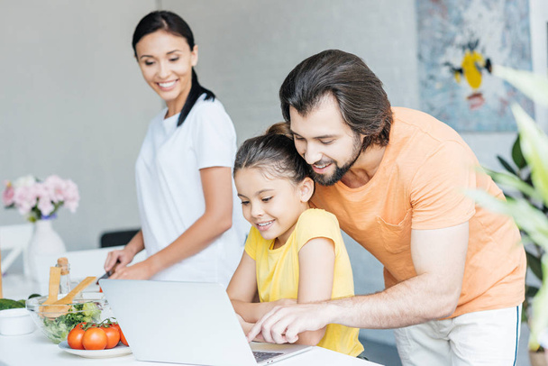 happy young family using laptop together at kitchen - 写真・画像